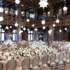 A grand hall filled with round-back wooden chairs with upholstered seats, arranged at elegantly decorated wedding reception tables with floral centerpieces and candles